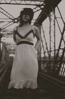 A sepia image of a woman standing on a bridge with railway tracks.