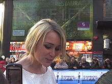 A smiling short-haired blond woman in a white top.