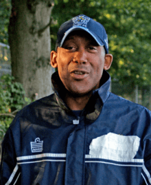 Head and upper torso of a middle-aged black man pictured outdoors wearing baseball cap and nylon jacket.