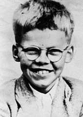 Head and shoulders monochrome photograph of a smiling short-haired young boy wearing spectacles.