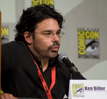 A man in a black shirt speaks into a microphone.