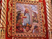 A painting on carved wood showing various people, among others: American Indians, a black person, two European-looking persons. The central figure is St. Paul, with a halo holding a book with red cover in his left and a sword in his right hand.