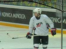An ice hockey player on the ice. He is wearing a white jersey with the letters "USA" on the front in red and blue.
