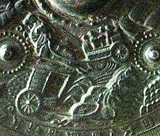 Detail of a metal object showing embossed scene of a horse-drawn chariot.