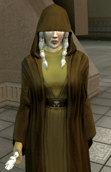 An elderly woman, Kreia, stands, wearing earth-tone robes. The top half of her face, along with her eyes, are covered by dark brown hood, part of another robe worn over her clothes. A braid of hair comes down from each side of her face, and her left hand is missing.