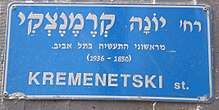 The blue Israeli street sign is in Hebrew. Translated to English it says: "Yonah Kremenetski, one of the first industrialists in Tel Aviv (1850-1936)."