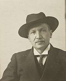 A picture of Kullervo Manner, chairman of the Finnish People's Delegation and last commander-in-chief of the Reds, looking straight at the camera with a suit and a hat on.