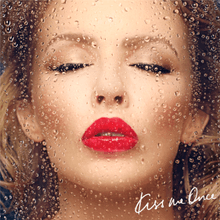 A face portrait of a woman (Kylie Minogue) kissing a clear glass screen, with water droplets running down. A blue-ish background is behind the woman, with the text "Kiss Me Once" present on the bottom right corner.