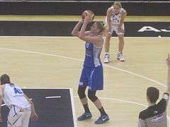 A basketball player lines up a penalty throw. She is wearing a blue top and baggy shorts.
