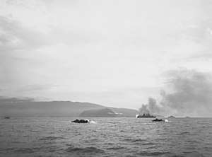 A harbor with a number of amphibious ships racing from battleships out to sea to the shore