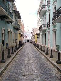 Buildings with wrought-iron balconies line a cobbled street.