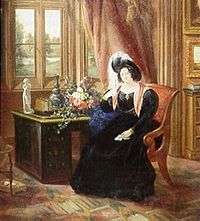 A colour picture of an 1833 painting of Lady Tyrconnell sitting in a brown covered chair while in an 1830s dark blue full dress gown with puffy sleeves, reddish scarf and a dark feathered round hat. She is sitting in the carpeted Gothic style Drawing room next to a brown desk and light red drappered window.