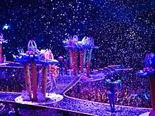 A faraway shot of a stage, with giant flowers and confetti raining.
