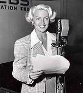 Woman in front of a microphone holding sheath of paper