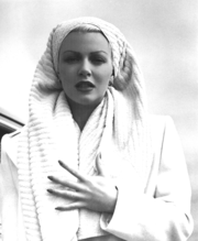 Woman in white wearing a towel on her head, clutching her chest