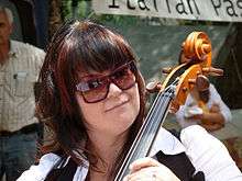 Lani Groves, a caucasian female with dark brown hair, wearing glasses and playing a cello.