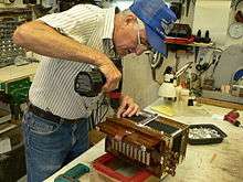 Larry Miller in a cap in his shop screwing a screw on a Cajun accordion.