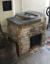 Photograph of a brick-lined laundry copper, with a round lid in the top and a grate below for the fire