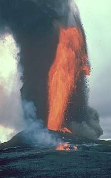 A jet of fluid lava spraying into the air on an island. Smoke rises behind it.