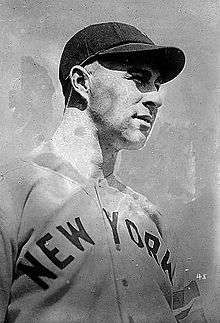 A black-and-white photo of a man in a white baseball jersey with "NEW YORK" across the chest in block letters and a dark baseball cap