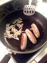 Three Lincolnshire sausages, with chopped onions in a frying pan with a spatula on a hob