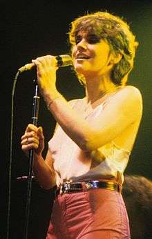 Linda Ronstadt, with short dark hair, singing onstage