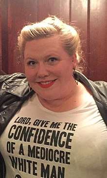 Lindy West wears a black jacket and white t-shirt printed with the words "Lord, give me the confidence of a mediocre white man."
