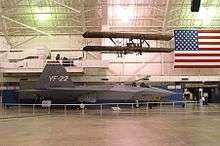 Starboard view of jet aircraft in museum among suspended aircraft and an American flag.