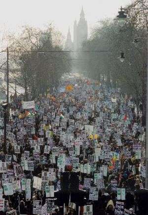 A large crowd, some of whom are carrying banners walks through London. The protest against the Iraq War, in London, February 2003, forms a backdrop to the events of Saturday.