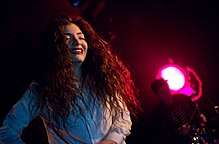 Lorde smiling as she performs on-stage in white attire