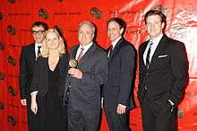 From left to right, Fred Armison, Amy Poehler, Lorne Michaels, Seth Meyers, and Jason Sudeikis stand in a line. Michaels holds an award.