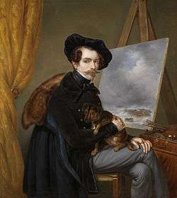 Louis Meijer seated with legs crossed while holding a dog in front of a painted canvas.
