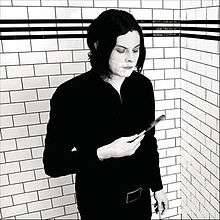 A grayscale picture of Jack White against a wall looking at a pen in his hand