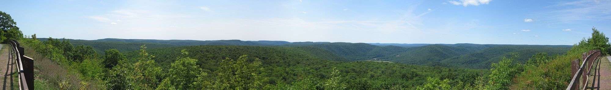 View from a fenced overlook of wooded low mountains whose peaks are all nearly the same height