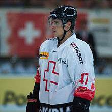 A Caucasian male ice hockey player shown from the knees up. He is wearing a red and white sweater with a black helmet.