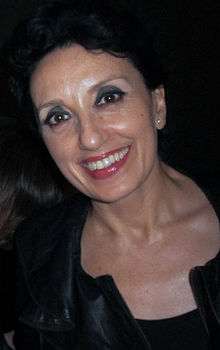 A woman with black hair is wearing a black dress and is facing the camera.