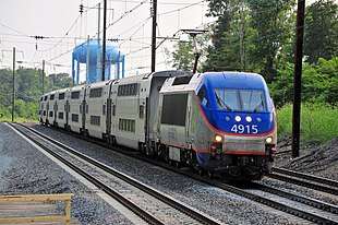 Blue and silver locomotive with orange striping pulling six bilevel locomotives on triple-track
