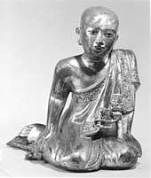 Wooden sculpture of monk sitting in a mermaid pose, reclining