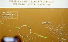 Brown background with white lines, dots, and labels depicting air routes, waypoints, and airports. Label in the top of the image reads: "Military radar plot from Pulau Perak to last plot at 02:22H." Green specks form a trail from bottom centre to left centre that was Flight 370. As the caption explains, the path is in two parts, with a white circle around the blank area between them and appears to highlight a section where the aircraft was not tracked by radar. Label at left end of flight path reads: "Time-02:22H 295R 200nm from Butterworth AB"