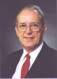 image of Mack Breazeale from 1997, smiling in a white shirt, red tie, and dark suit coat