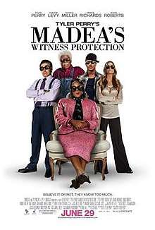 The poster shows five people, four standing and one sitting in chair wearing black sunglasses in a white background. Text at the top of the poster reveals the title. Text at the bottom of the poster reveals the production credits, rating and release date.