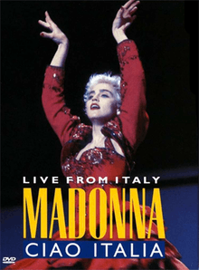 Madonna in short cropped hair, wearing a red flamenco dress. She puts up both of her hands above her head