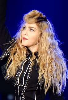 Madonna in a bejeweled jacket with blond hair in curls around her looking towards her right