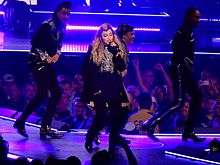 Madonna singing on a blue-lit stage in black costumes, surrounded by dancers