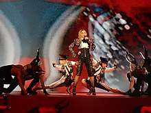 Madonna standing in the middle of a stage. Her dancers flank her near the stage floor.