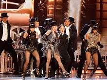 Madonna in a shiny dress, flanked by male dancers in coattails.