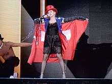 Madonna wearing a red flag around herself, and a red tophat singing onstage.