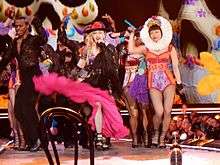 Madonna and her dancers in colorful cloths dancing onstage.