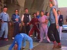 Image shows a group of youngsters on the pavement of a street with Madonna dancing beside them.
