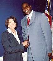 A middle-aged Caucasian woman shakes the hand of a tall black man.
